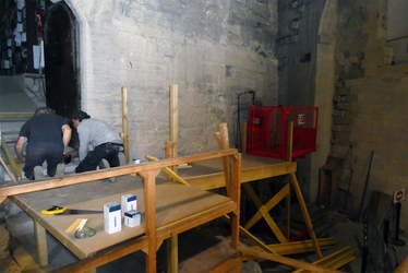 Deux hommes accroupis et de dos fabriquent un plan incliné devant la façade d'un vieux bâtiment - Agrandir l'image (fenêtre modale)