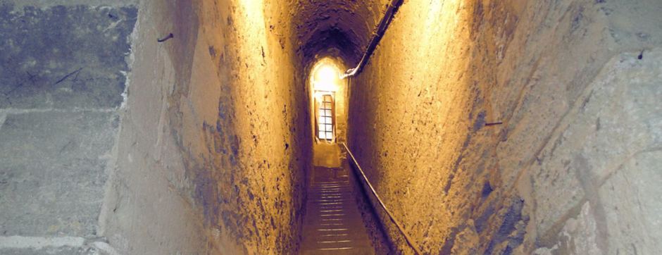 Escalier sombre et étroit, vaguement éclairé par une petite fenêtre poussièreuse à carreaux