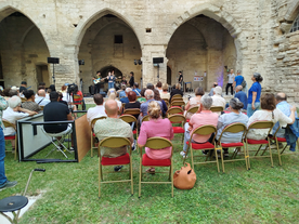 Vue sur une cour engazonnée, ceinte d'arches médiévales, un public assiste à un concert - Agrandir l'image, .JPG 1,1 MB (fenêtre modale)