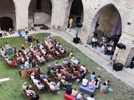 Vue à la tombée de la nuit sur une cour engazonnée, ceinte d'arches médiévales, un public assiste à un concert - Agrandir l'image, .JPG 1,1 MB (fenêtre modale)
