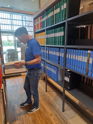 Une personne consulte un ouvrage entre deux rayonnages bois et métail d'une bibliothèque