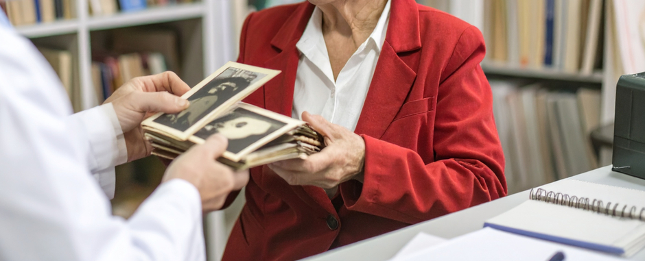Un homme en blouse blanche reçoit d'une dame vétue de rouge des photos